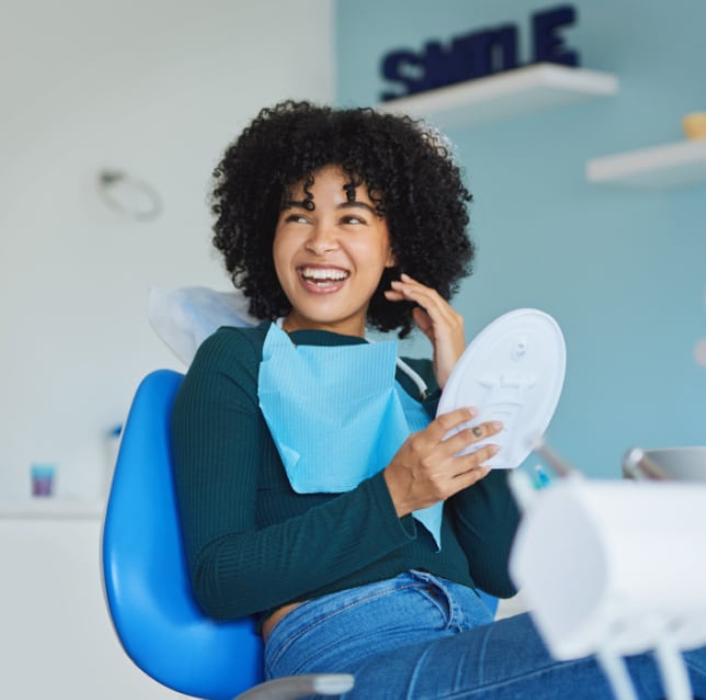 Smiling woman holding dental mirror in modern blue dental office setting.
