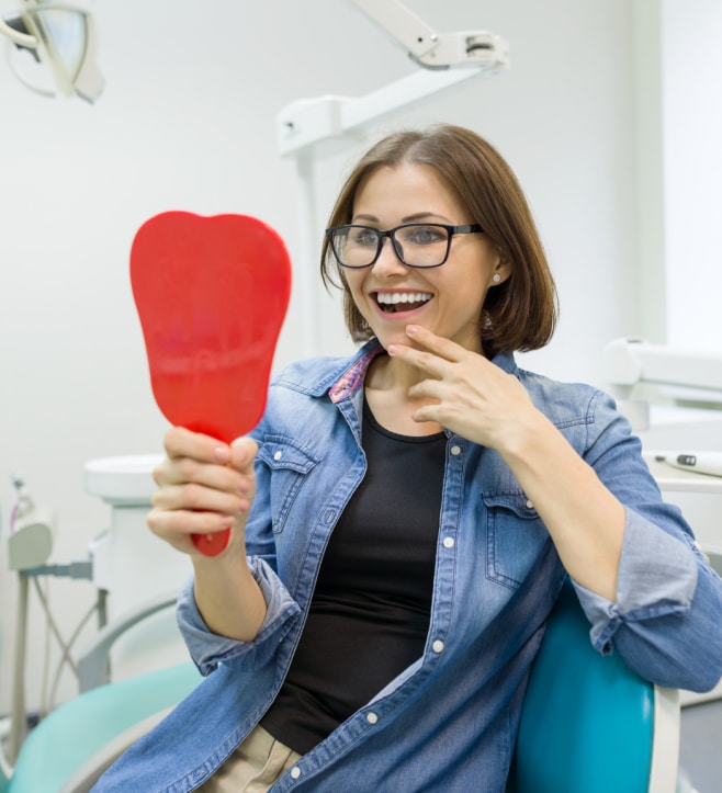 Dentist holding red mouth model in dental office, smiling at camera