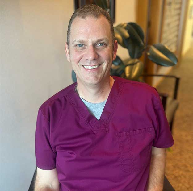 Smiling male dentist in purple scrubs at dental office.